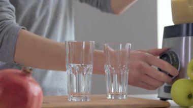 Mutfakta, farklı meyvelerden lezzetli meyve püresi hazırlamak için blender 'da meyve çizen genç bir sporcu. Bardaklara taze meyve suyu döküyor.