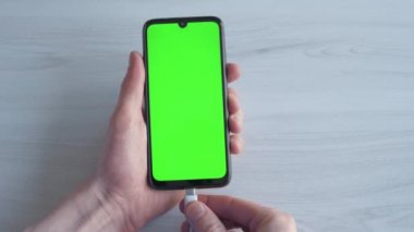 Şarj edilen cep telefonu, akıllı telefon. Adam ahşap arka planda elinde bir cep telefonu tutuyor. Yükleyici USB C şarj aygıtı işlemine bağlanılıyor.