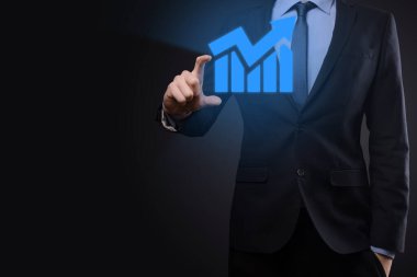 İş adamı elinde tablet tutuyor ve karanlık zemin üzerinde ok bulunan istatistik, grafik ve grafiklerin büyüyen sanal hologramını gösteriyor. Borsa. İş büyümesi, planlama ve strateji kavramı