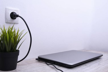 Laptop, bilgisayar duvarın yanındaki bir masada 220 voltluk bir prizden şarj oluyor. Enerji, birikim