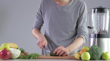 Mutfaktaki mutfak masasındaki genç bir adam meyve suyu için salatalık kesiyor. Karıştırıcıda smoothie pişiriyorum.