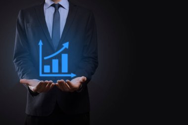 İş adamı elinde tablet tutuyor ve karanlık zemin üzerinde ok bulunan istatistik, grafik ve grafiklerin büyüyen sanal hologramını gösteriyor. Borsa. İş büyümesi, planlama ve strateji kavramı