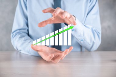 İş adamı elinde pozitif kar artışı olan bir grafik tutuyor. Grafik büyümesi ve grafik artışı işlerinde olumlu göstergeler. Daha kârlı ve büyüyen.