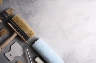 Gri beton arka planda boya yapmak için macun, fırça ve silindirler kullanılıyor. Üst görünüm