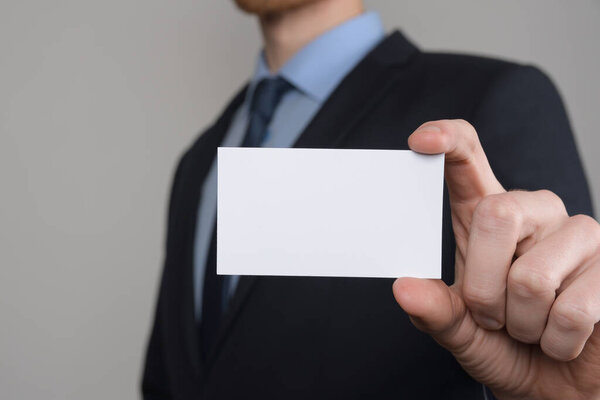 Бизнесмен, рука бизнесмена показывает визитную карточку - крупный план на сером фоне. Покажите чистый лист бумаги. Карточка посещения.