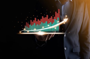 İş adamı, karanlık arka planda okları olan, istatistik, grafik ve grafiklerin büyüyen sanal bir hologramını tutuyor ve gösteriyor. Borsa. İş büyümesi, planlama ve strateji kavramı