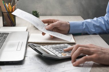 Hesap makinesi ve yazı makinesi kullanan bir adam ev ofisinin maliyet ve vergilerini hesaplayarak not alır. İşadamı iş yerinde evrak işleriyle uğraşıyor.