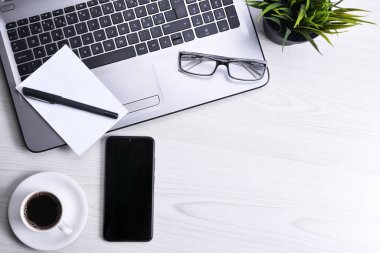 Ofis çalışma alanının en üst görüntüsü, dizüstü bilgisayarı, klavyesi, gözlükleri, telefonu ve bir fincan kahvesi olan tahta masa masası..