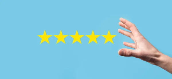 Man holds smart phone in hands and gives positive rating, icon five star symbol to increase rating of company concept on blue background.Customer service experience and business satisfaction survey