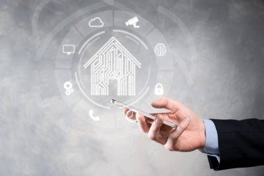 İş adamı ev ikonunu tutuyor. Marketin ev kontrollü, akıllı ev ve ev otomasyon uygulaması konsepti. PCB tasarımı ve akıllı telefonu olan kişi. Yenilik teknolojisi internet ağı kavramı