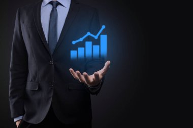 İş adamı elinde tablet tutuyor ve karanlık zemin üzerinde ok bulunan istatistik, grafik ve grafiklerin büyüyen sanal hologramını gösteriyor. Borsa. İş büyümesi, planlama ve strateji kavramı