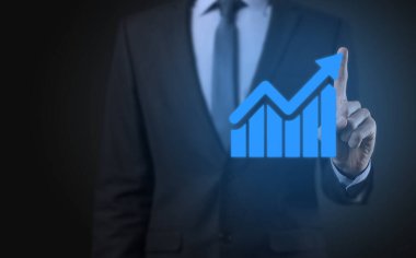 İş adamı elinde tablet tutuyor ve karanlık zemin üzerinde ok bulunan istatistik, grafik ve grafiklerin büyüyen sanal hologramını gösteriyor. Borsa. İş büyümesi, planlama ve strateji kavramı