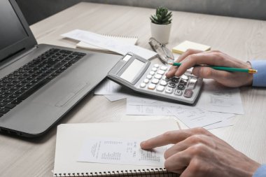 Hesap makinesi ve yazı makinesi kullanan bir adam ev ofisinin maliyet ve vergilerini hesaplayarak not alır. İşadamı iş yerinde evrak işleriyle uğraşıyor.