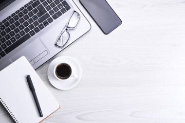 Ofis çalışma alanının en üst görüntüsü, dizüstü bilgisayarı, klavye kalemi, gözlükleri, telefonu, defteri ve kahveyi olan ahşap masa masası..