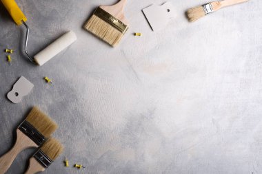Gri beton arka planda boya yapmak için macun, fırça ve silindirler kullanılıyor. Üst görünüm