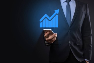 İş adamı elinde tablet tutuyor ve karanlık zemin üzerinde ok bulunan istatistik, grafik ve grafiklerin büyüyen sanal hologramını gösteriyor. Borsa. İş büyümesi, planlama ve strateji kavramı