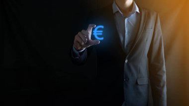 İş adamı, para sikkesi ikonlarını koyu tonda arka planda tutar iş yatırımları ve finans için büyüyen para kavramına sahiptir..