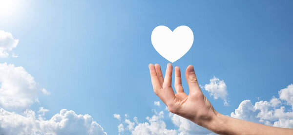 Male hand holding heart , like icon on blue background. Kindness, charity, pure love and compassion concept.Banner with copy space.