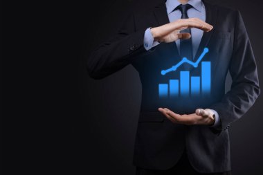 İş adamı elinde tablet tutuyor ve karanlık zemin üzerinde ok bulunan istatistik, grafik ve grafiklerin büyüyen sanal hologramını gösteriyor. Borsa. İş büyümesi, planlama ve strateji kavramı