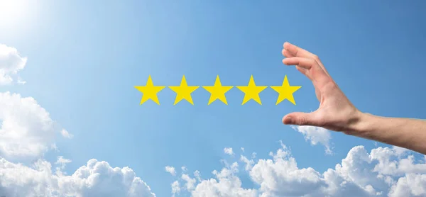Man holds smart phone in hands and gives positive rating, icon five star symbol to increase rating of company concept on blue background.Customer service experience and business satisfaction survey