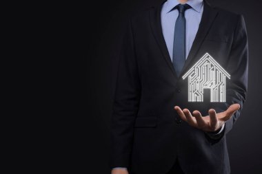 İş adamı ev ikonunu tutuyor. Marketin ev kontrollü, akıllı ev ve ev otomasyon uygulaması konsepti. PCB tasarımı ve akıllı telefonu olan kişi. Yenilik teknolojisi internet ağı kavramı