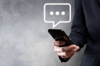 Elinde mesaj ikonu tutan bir iş adamı, elinde baloncuklu konuşma tebligat işareti var. Sohbet simgesi, SMS simgesi, yorum simgesi, konuşma baloncukları.