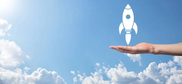 Male hand holding rocket icon that takes off, launch on blue background. rocket is launching and flying out, Business start up, Icon marketing on modern virtual interface.Start up concept