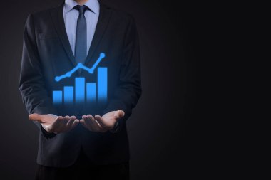 İş adamı elinde tablet tutuyor ve karanlık zemin üzerinde ok bulunan istatistik, grafik ve grafiklerin büyüyen sanal hologramını gösteriyor. Borsa. İş büyümesi, planlama ve strateji kavramı