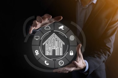 İş adamı ev ikonunu tutuyor. Marketin ev kontrollü, akıllı ev ve ev otomasyon uygulaması konsepti. PCB tasarımı ve akıllı telefonu olan kişi. Yenilik teknolojisi internet ağı kavramı