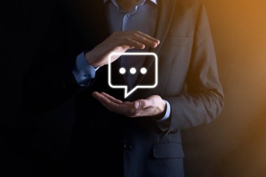 Elinde mesaj ikonu tutan bir iş adamı, elinde baloncuklu konuşma tebligat işareti var. Sohbet simgesi, SMS simgesi, yorum simgesi, konuşma baloncukları.