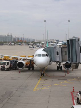 12.10.2025 Münih, Almanya: Meşgul havalimanı pistinde yer desteği ile Jet Köprüsü 'ne Bağlı Kapıdaki Uçak. Ticari bir uçak, yer ekibi olarak bir jet köprüsüne bağlı bir kapıda oturur.