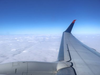 Yolcu jet kanadı bulutlar denizi üzerinde berrak mavi havayı keser, yolculuk, özgürlük ve uçuş macerasını çağrıştıran sakin, yüksek irtifa perspektifi sunar..