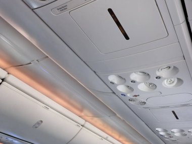 Modern bir uçak kabininin içerisine özel bir bakış açısı, yukarıdaki konsolu ışıklar, havalandırmalar ve kontrollerle aydınlatıyor. Seyahat, uçuş konforu ve uçuş konforu temaları için ideal.