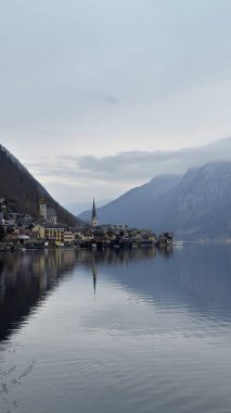 Hallstatt, Avusturya - 16 Şubat 2025: Hallstatt Avusturya 'nın manzaralı manzarası sergilenen dağlar ve resimli köy manzarasını yansıtan sakin bir göl