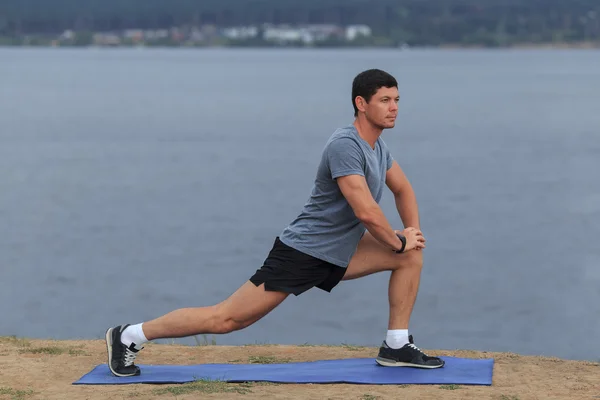 Man doing yoga outdoor. Young man practicing yoga fitness exercise outdoor at beautiful sea. Meditation and relaxatio.