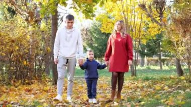 Anne ve baba ve oğul sonbahar parkı boyunca el ele yürür.
