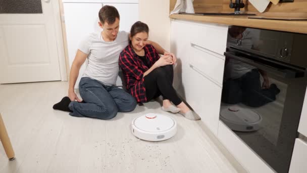 Young couple of man and woman watching robot vacuum cleaner while sitting on floor — Stock Video