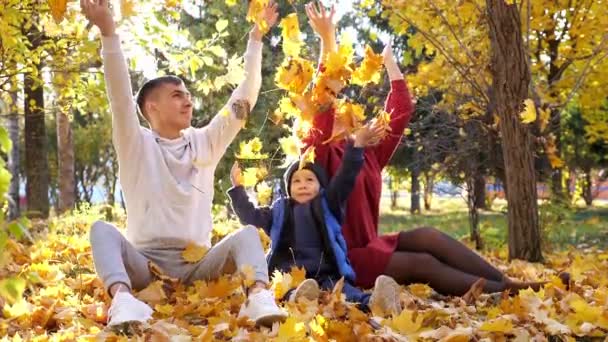 Preciosa familia arroja hojas amarillas secas en el soleado parque de otoño — Vídeo de stock