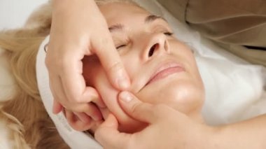 Yetenekli güzellik salonu çalışanı olgun kadın yüzüne masaj yapar.