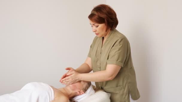 Ervaren masseur massages jonge vrouw gezicht in salon — Stockvideo