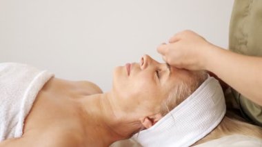 Uzman, güzellik salonunda bir kadına yüz ve boyun masajı yapıyor.