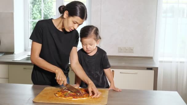 Annem küçük kızın önünde yeni pişmiş pizza keser. — Stok video