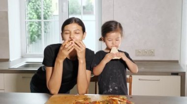 Aç anne ve küçük kız lezzetli pizza dilimleri yiyorlar.