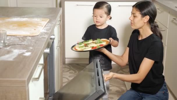 Klein meisje helpt mam zet heerlijke pizza in moderne oven — Stockvideo
