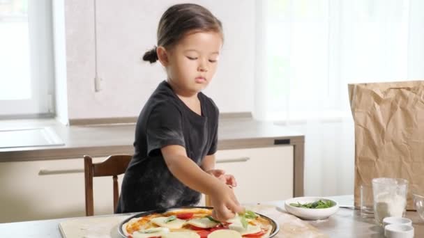 Niña prepara pizza poniendo albahaca en la base — Vídeo de stock