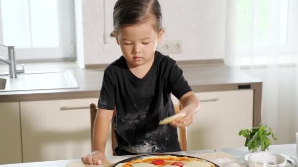Leuke peuter zet grote plakjes kaas op elastische pizza basis — Stockvideo