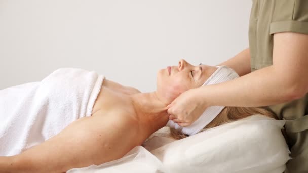 Schoonheidssalon therapeut in jas massages liegen vrouw wangen — Stockvideo