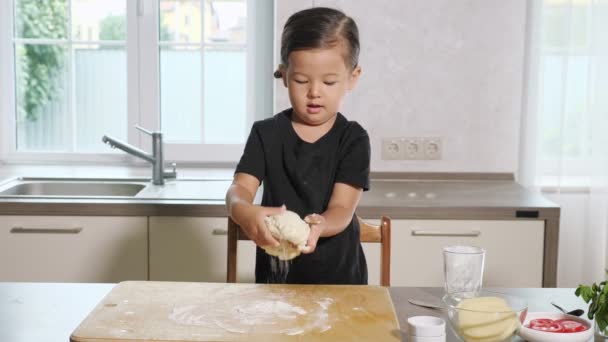 Liten flicka stretching deg på träskiva i köket — Stockvideo