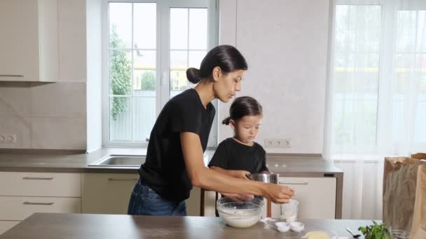 Мама и дочка просеивают муку через решето в миску на кухне. — стоковое видео