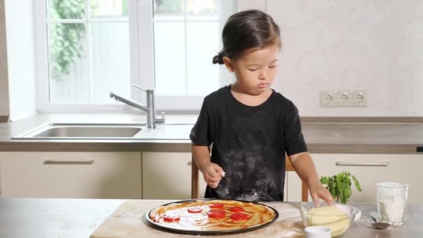 Маленькая девочка кладет помидоры на тесто, размазанные соусом — стоковое видео